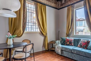 Un salon confortable avec un canapé, une table à manger et des chaises, ainsi qu’une fenêtre avec des rideaux.
