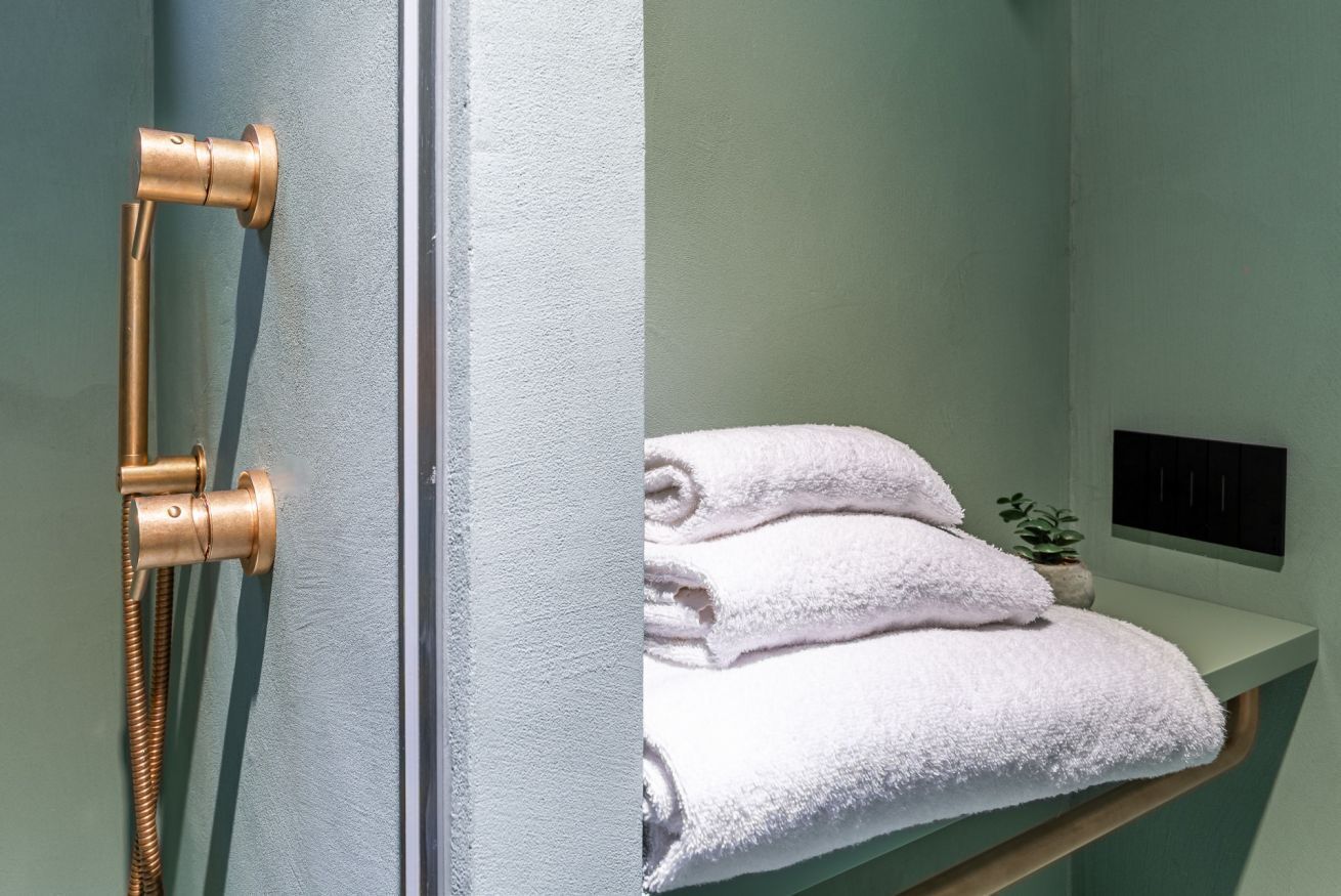 A bathroom with a gold shower head, a white towel rack, and a small potted plant.
