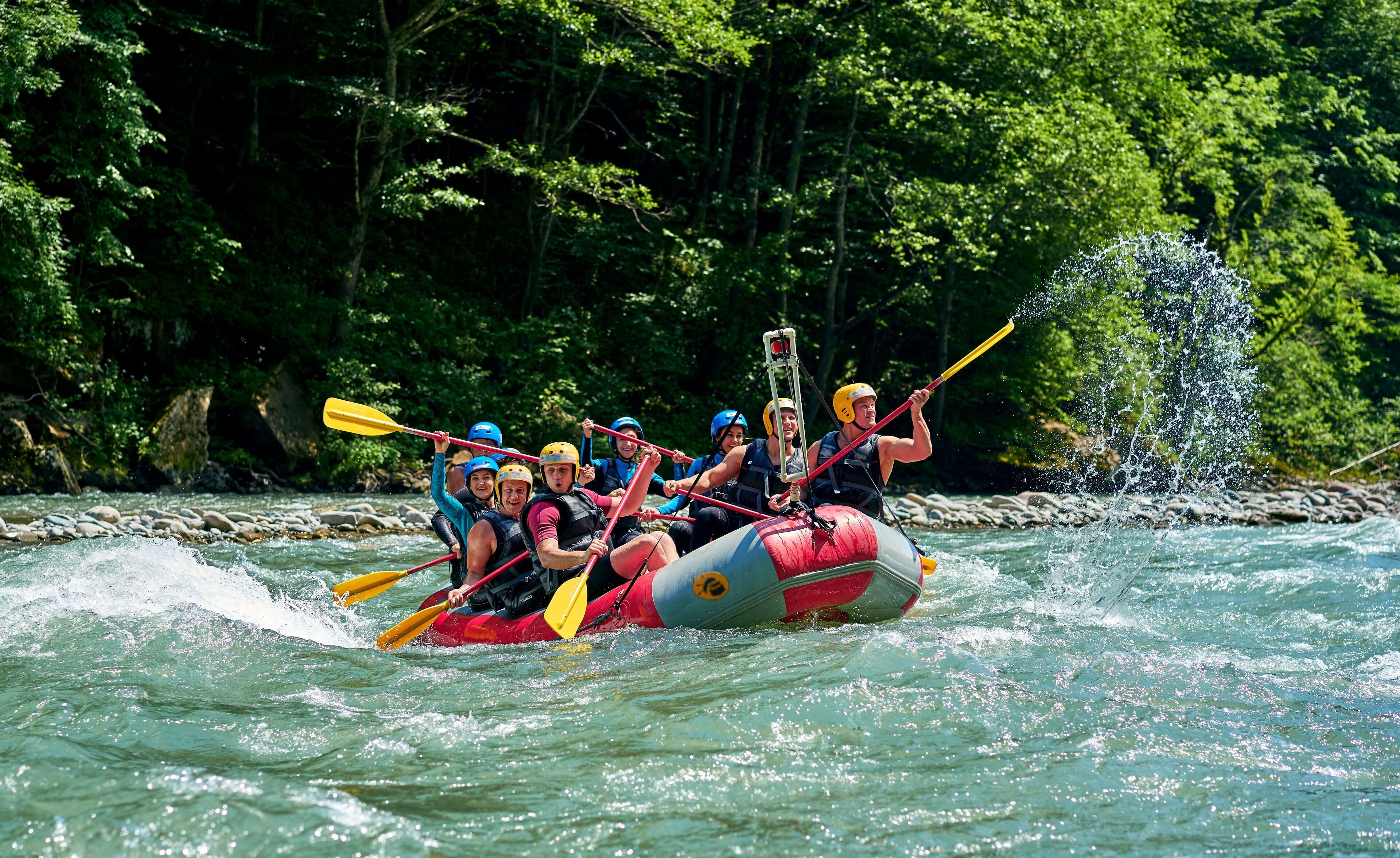 A group of people in a raft navigating a river surrounded by dense forest.