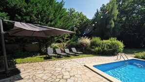 Une terrasse en pierre avec une piscine, des chaises longues et un espace abrité doté d’un auvent.