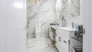 A modern bathroom with marble walls, a glass shower enclosure, and a gold chandelier. - Modern Catskills Mountain Retreat with Rooftop Hot Tub on 22 Private Acres (Denver)
