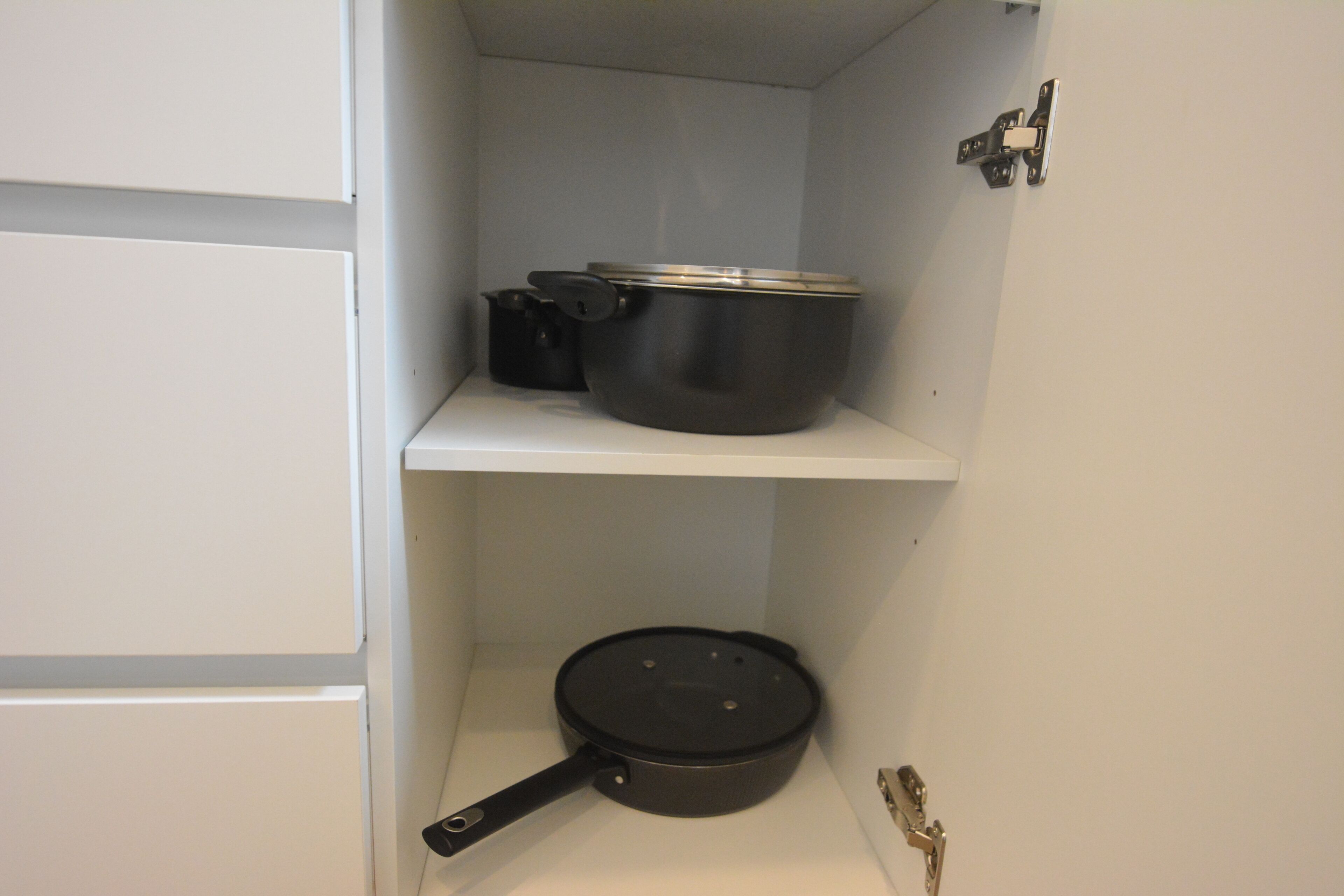A kitchen with white cabinets and a shelf holding a black pot and pan.
