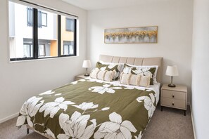 A bedroom with a bed, two bedside tables, a window, and a painting on the wall.