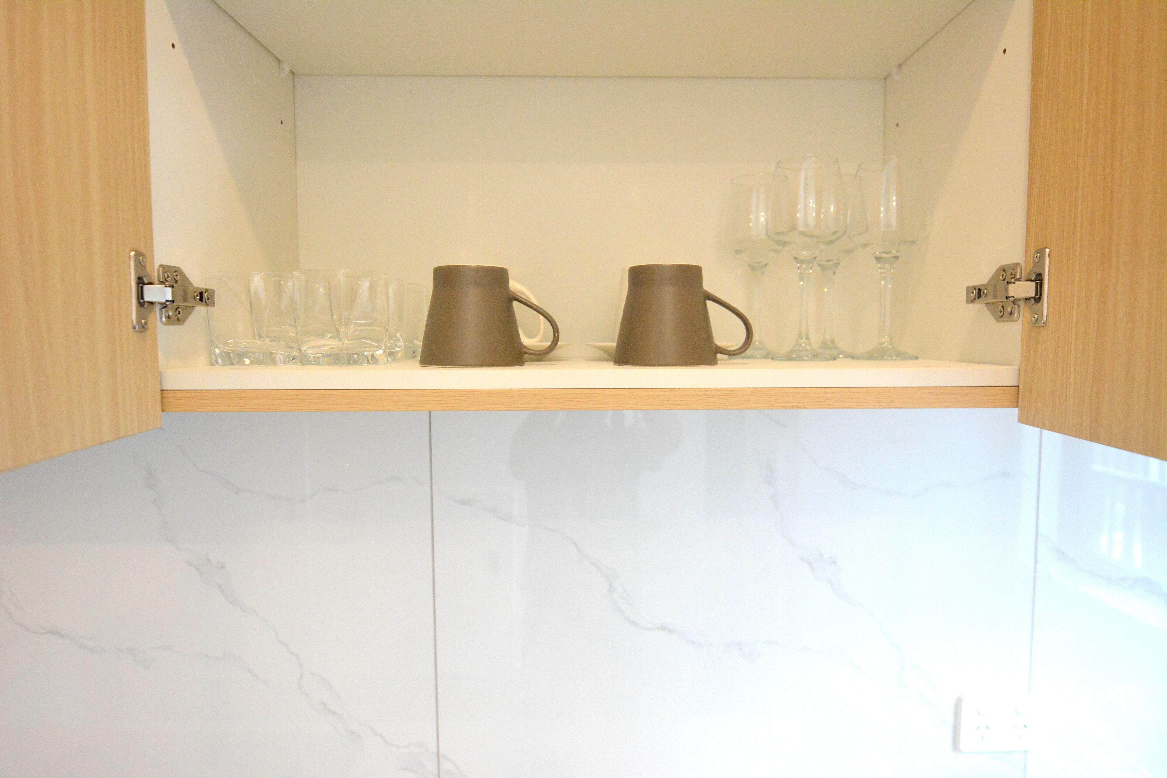 A kitchen with a marble countertop, two brown mugs, and several wine glasses.