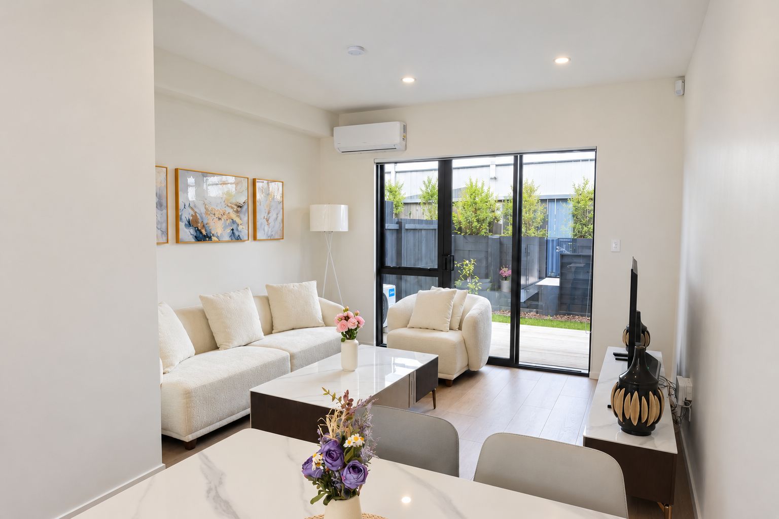 A modern living room with a sofa, coffee table, and a dining area with chairs and a vase of flowers.