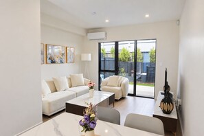 A modern living room with a sofa, coffee table, and a dining area with chairs and a vase of flowers.