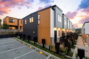 A modern residential building with a covered outdoor area and a parking lot. - Family-Friendly New 3BR Townhouse | Gated Community & Secure Parking (Glen Eden)