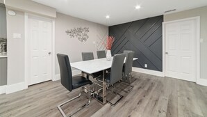 Ein Essbereich mit weißem Tisch und schwarzen Stühlen, einer Dekoration an der Wand und einem geometrischen Wandmuster.