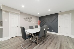 Un espace repas avec une table blanche et des chaises noires, un élément décoratif mural et un motif géométrique sur le mur.