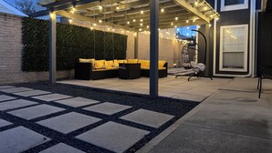 Ein überdachter Patio-Bereich mit Gartenmöbeln, Lichterketten und einer Pergola.