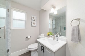 Ein Badezimmer mit Toilette, Waschbecken, Spiegel, Dusche und einem Fenster.