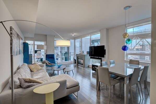 A modern living room with a sofa, a dining table with chairs, a TV, and a fireplace. - LUXURY BEACH AVE 2 BED SUITE (Vancouver)