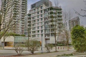 A modern high-rise building with multiple balconies and large windows, surrounded by trees and a clear sky. - LUXURY BEACH AVE 2 BED SUITE (Vancouver)