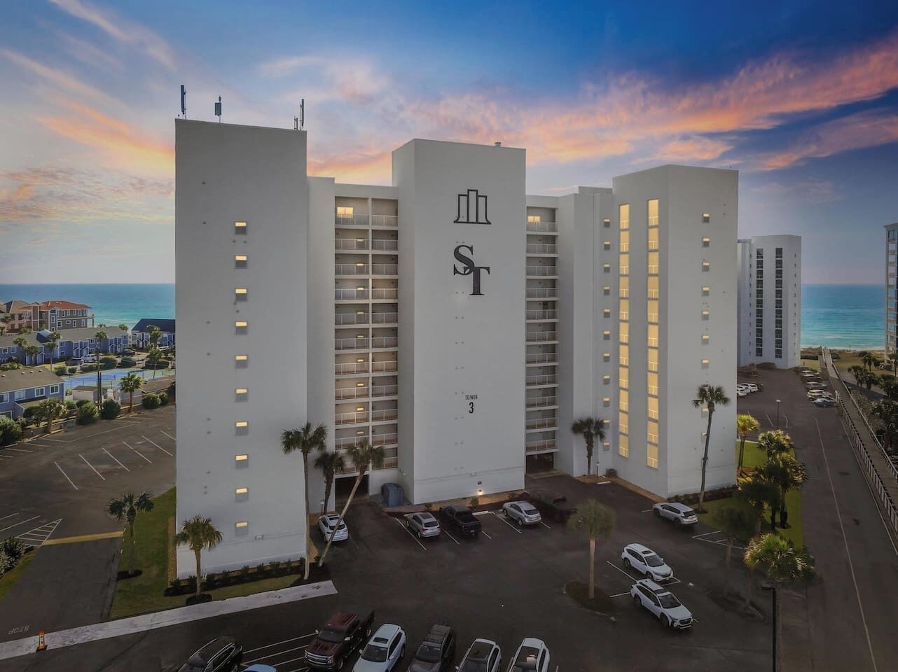 Et hotel med flere etager, et tydeligt 'ST'-logo, en parkeringsplads og udsigt over havet.