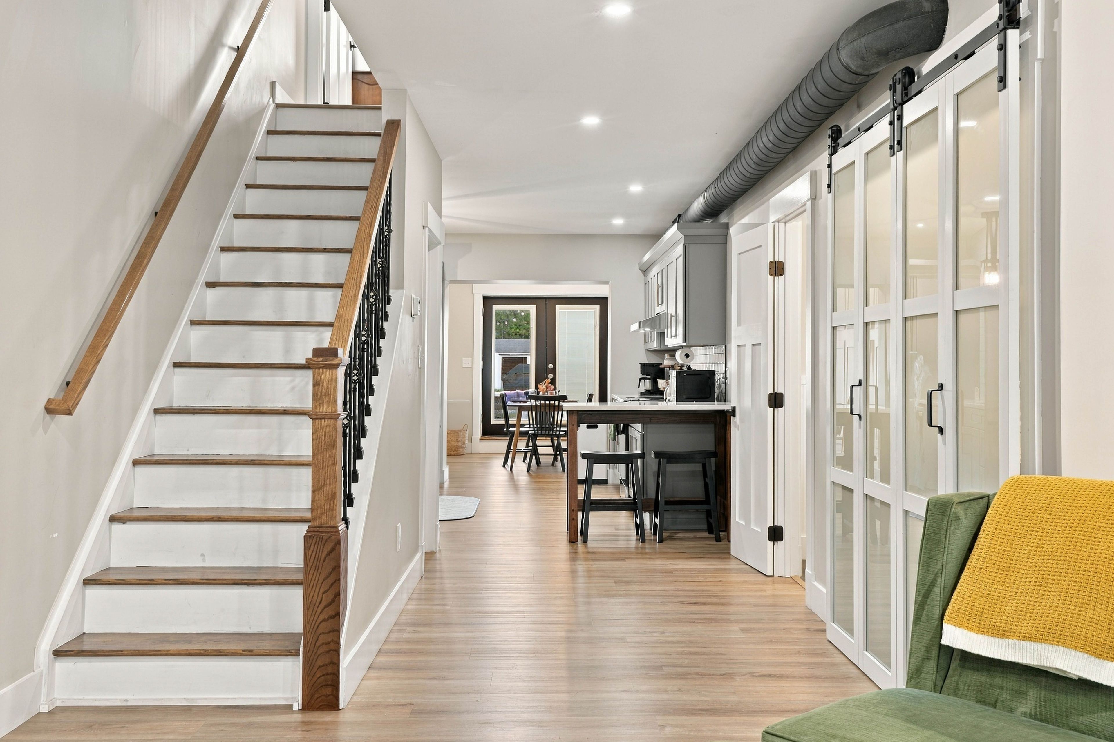 A staircase with wooden steps and a handrail, leading to a kitchen area with cabinets and a dining table.