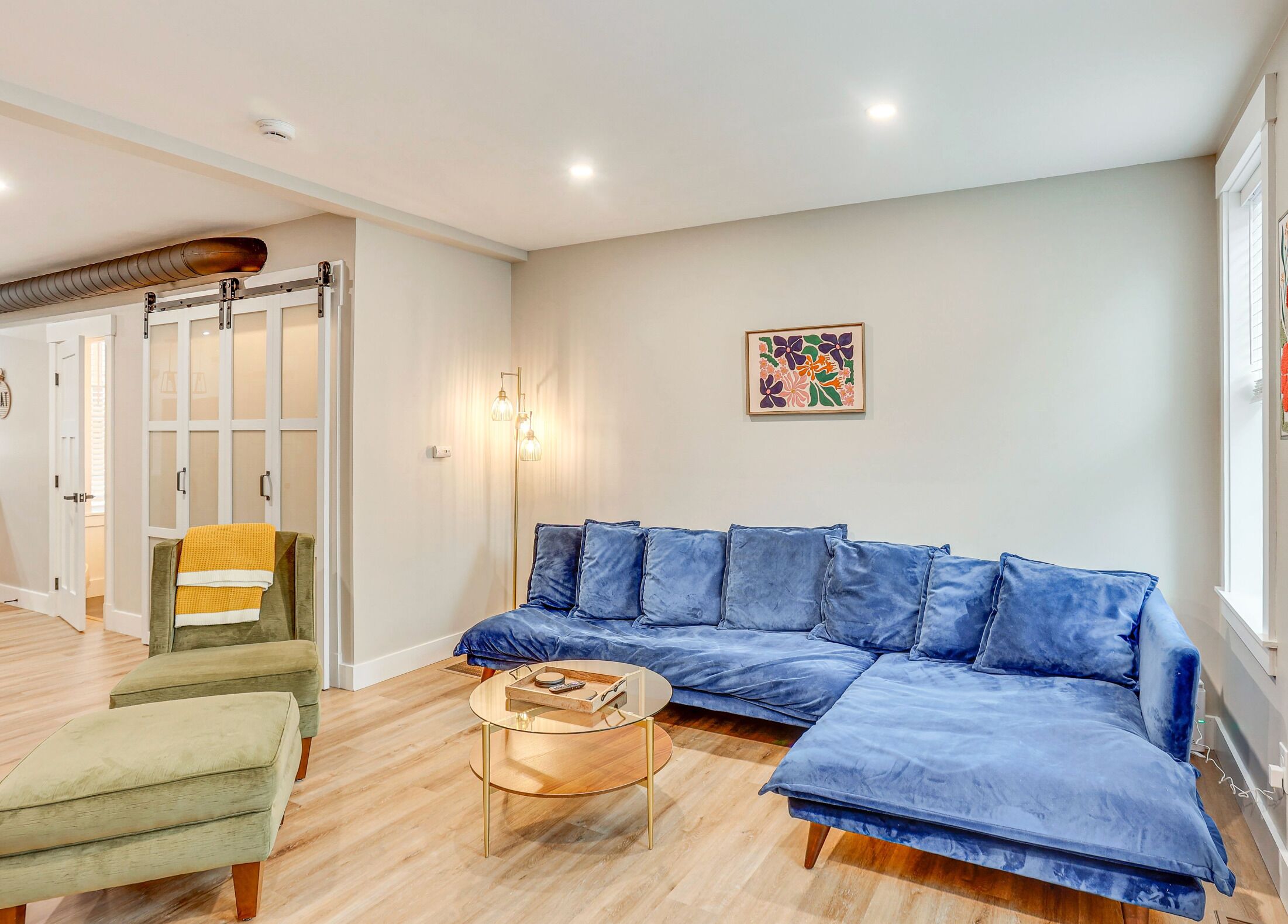 Een moderne woonkamer met een blauwe bank, een groene fauteuil en een glazen salontafel.