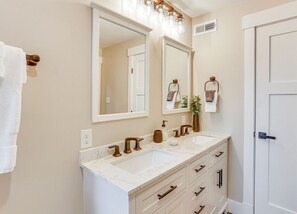 Un baño con dos lavamanos, un espejo grande y una puerta blanca.