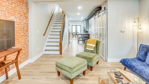 Ein geräumiges Wohnzimmer mit einer Holzbank, einem grünen Hocker und einem blauen Sofa. Eine Treppe führt zu einer oberen Ebene.