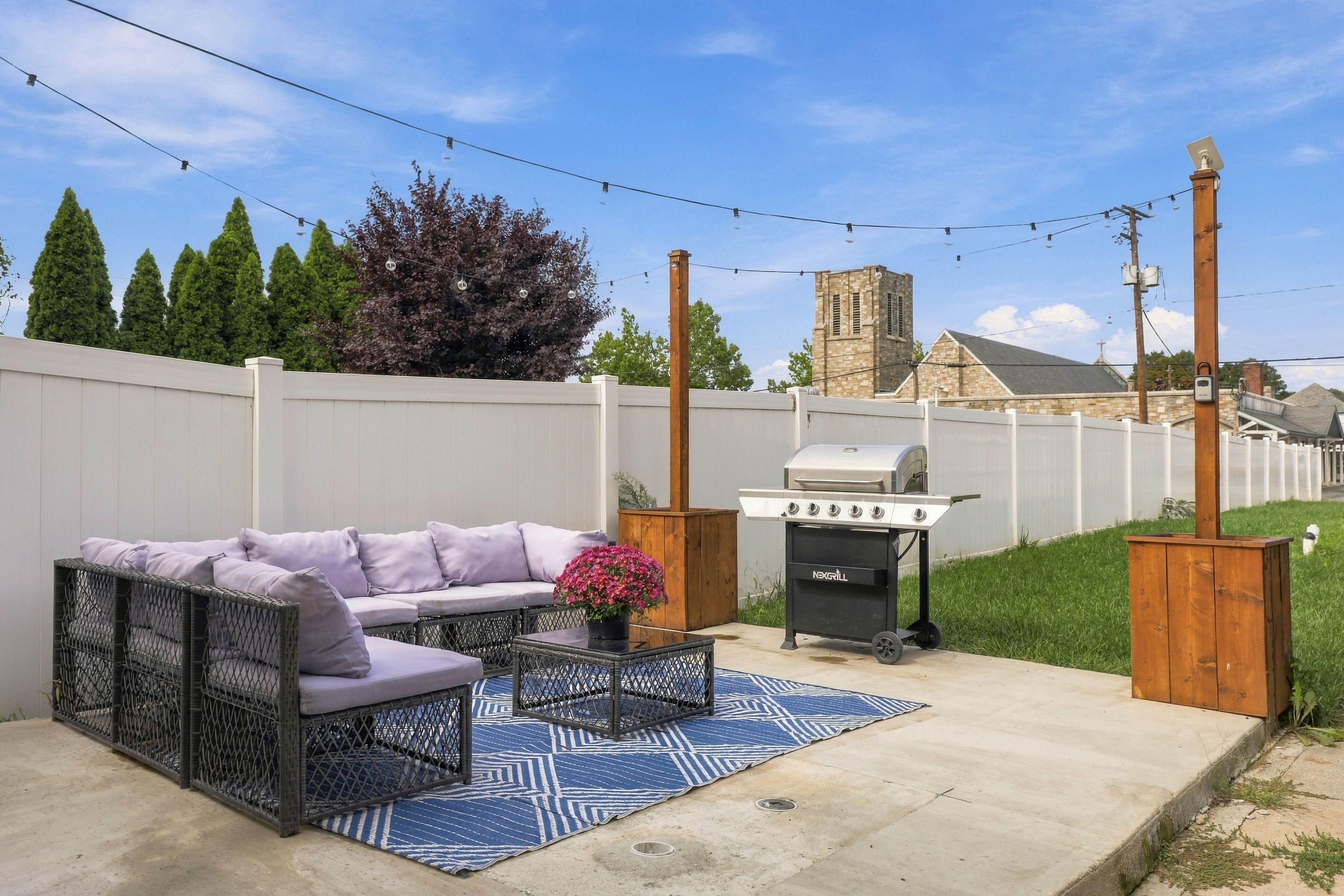 A backyard with a patio set, a grill, and a white fence.