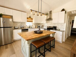 A modern kitchen with a central island, stainless steel appliances, and pendant lighting. - Coastal Cottage, Marsh & Intracoastal Views, 5-Min Walk to Private Beach Access  (Holden Beach)