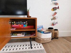 A wooden cabinet with board games, a woven basket, and decorative fish on the wall. - Coastal Cottage, Marsh & Intracoastal Views, 5-Min Walk to Private Beach Access  (Holden Beach)