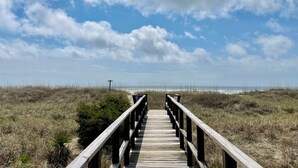 Une promenade en bois menant à la plage, avec un ciel dégagé au-dessus.