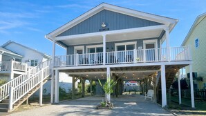 Une maison à deux étages située en bord de mer, dotée d’un porche couvert, d’un escalier et d’un petit jardin.