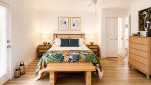 Une chambre à coucher comprenant un lit, des tables de chevet, un banc, une commode et un ventilateur de plafond.