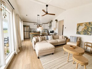 Een ruime woonkamer met een bank, een eettafel en een keuken op de achtergrond.