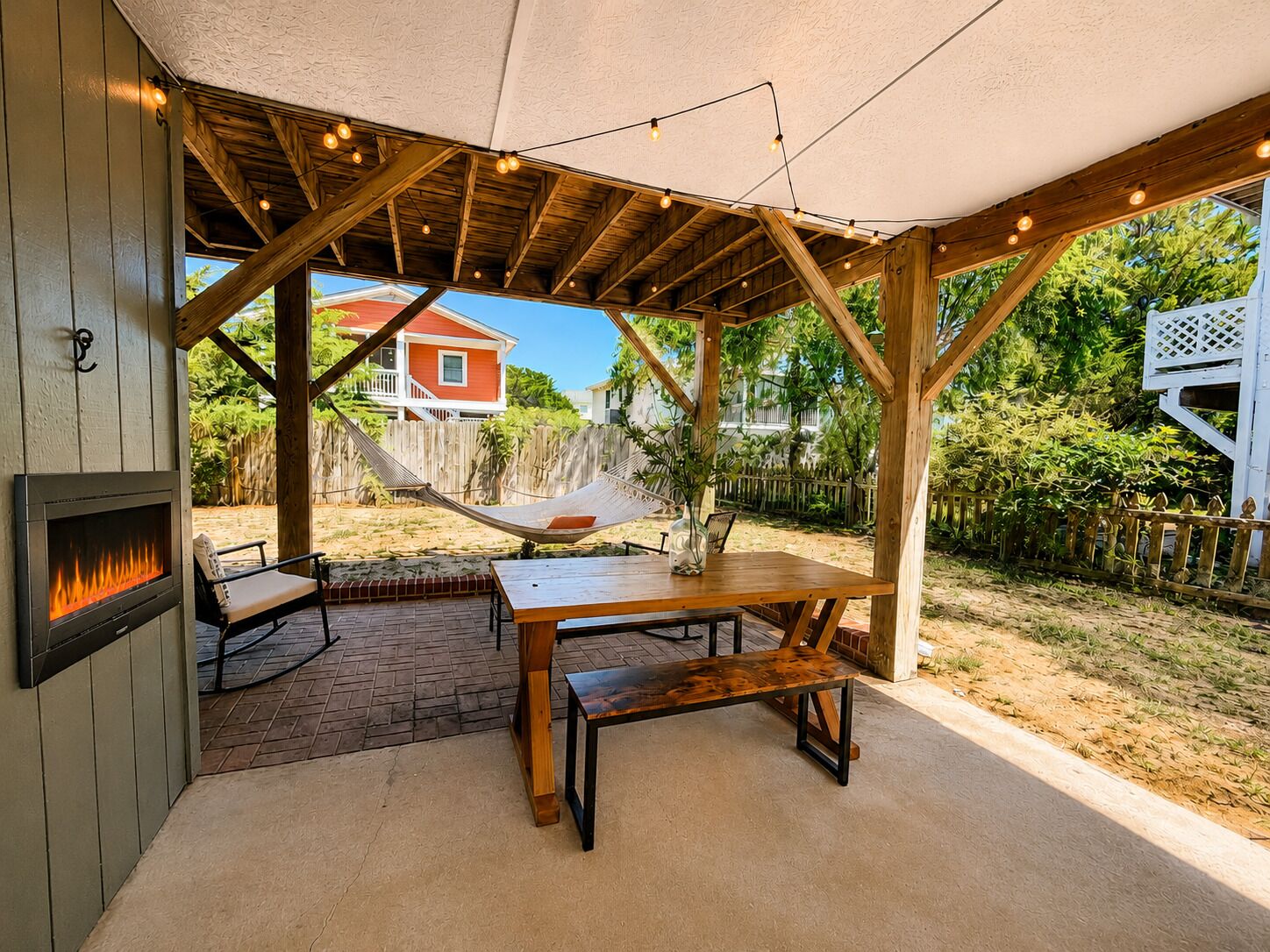 Un patio techado al aire libre con chimenea, muebles de madera y una hamaca.
