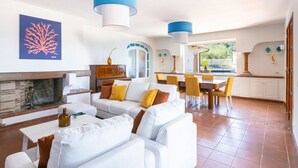 Ein geräumiger Wohnbereich mit Kamin, weißen Sofas, gelben Sesseln und einem Esstisch.