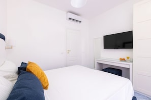 A hotel room with a bed, a desk with a flat-screen TV, a white wardrobe, and an air conditioning unit. - Seaview Luxury Villa with terrace, gym, jacuzzi, pool & bbq (Massa Lubrense)