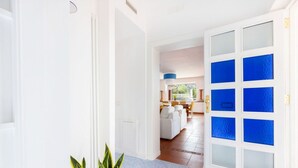 Ein Flur mit einer weißen Tür mit blauen Glaselementen, der zu einem Essbereich mit weißem Tisch und Stühlen führt.