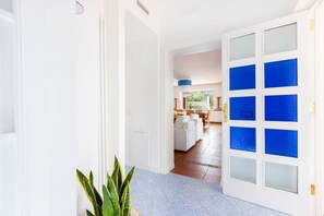 A hallway with a white door with blue glass panels, leading to a dining area with a white table and chairs. - Seaview Luxury Villa with terrace, gym, jacuzzi, pool & bbq (Massa Lubrense)
