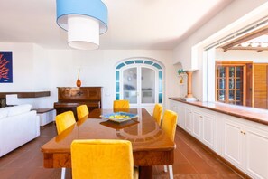 A dining area with a wooden table and yellow chairs, a white sofa, and a blue lamp. - Seaview Luxury Villa with terrace, gym, jacuzzi, pool & bbq (Massa Lubrense)