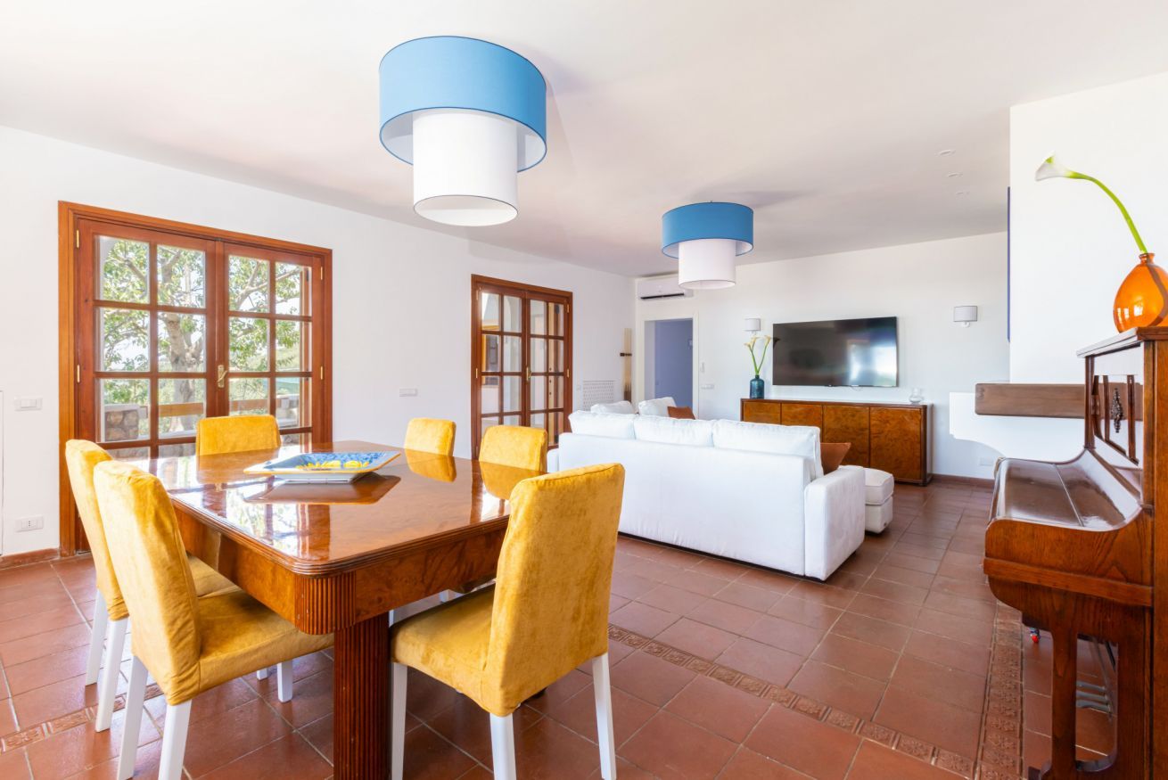 A spacious living room with a white sofa, a dining table with yellow chairs, and a TV.