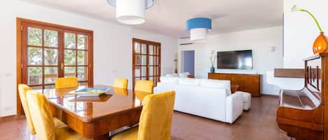 A spacious living room with a white sofa, a dining table with yellow chairs, and a TV.