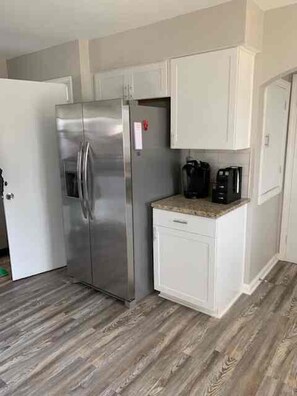 A compact kitchen with a stainless steel refrigerator, a coffee maker, and a white cabinet. - Brick Ranch On A Quiet Street In Historic Bedford (Bedford)