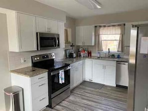 A modern kitchen with white cabinetry, a stainless steel refrigerator, and a microwave. - Brick Ranch On A Quiet Street In Historic Bedford (Bedford)