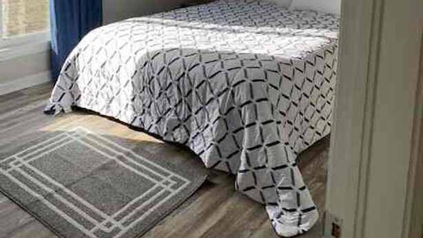 Een slaapkamer met een bed, een raam met gordijnen, een schilderij aan de muur en een vloerkleed.