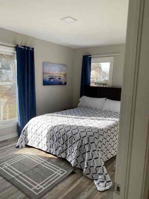 A bedroom with a bed, a window with curtains, a painting on the wall, and a rug on the floor. - Brick Ranch On A Quiet Street In Historic Bedford (Bedford)