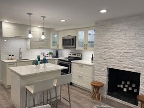 A modern kitchen with white cabinetry, a central island with bar stools, a built-in oven, and a stone accent wall. - Charming & Spotless 1-bedroom Historic Capitol Hill Walkers Paradise! (Washington DC)