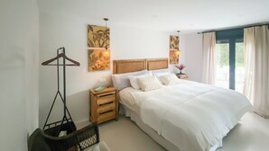 Une chambre d’hôtel avec un grand lit, une table de chevet en bois, un porte-manteau mural et des œuvres d’art accrochées aux murs.