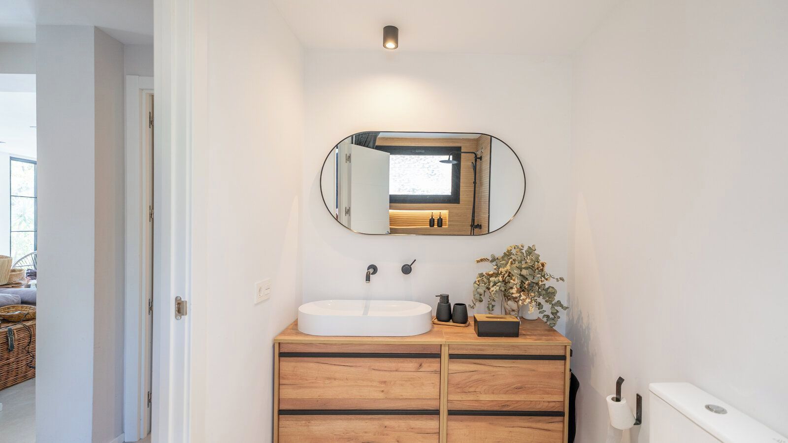 A bathroom with a white sink, wooden vanity, a mirror, and a potted plant.