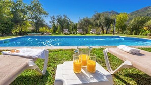 A poolside area with lounge chairs, a table with a pitcher of orange juice, and a clear view of the pool. - Los Cidrones Ubrique by Ruralidays (Cádiz)