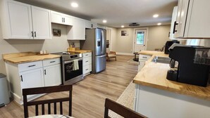 Una cocina compacta con armarios blancos, un refrigerador de acero inoxidable, un horno empotrado y una cafetera.