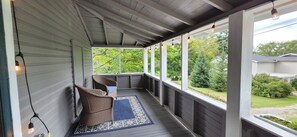 A covered porch with wicker chairs and a blue patterned rug.