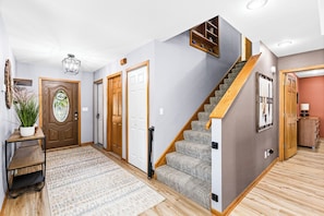 Un escalier avec des marches en bois et une rampe, une porte en bois avec un panneau de verre, et un tapis à motifs sur le sol.