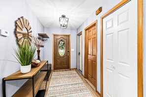 Un couloir avec un banc en bois, une plante en pot, un miroir décoratif, une porte ornée d’un vitrail et un tapis à motifs.