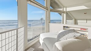 Un dormitorio con una ventana grande con vista a una playa, una cama y una pequeña zona de escritorio.
